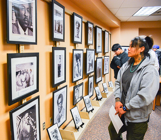 woman stands in front of a collection of photographs at a gallery.