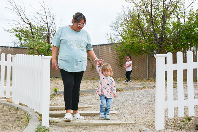 Teacher Roslind Joe holds 2-year-old NikiAnn Hudgeons’ hand while walking down the stairs as 21-month-old Jace Willie plays in the background at Bright Futures Daycare, located on The University of New Mexico-Gallup campus, on May 1, 2025.